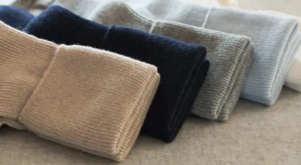 Gestapelte Mützen in Beige, Dunkelblau, Grau und Hellblau. So pflegt man Kaschmir, damit er lange schön bleibt.