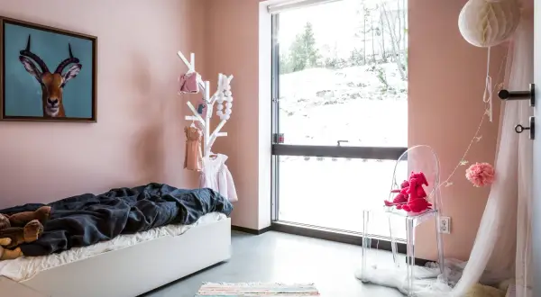 Ein gemütliches Kinderzimmer mit einer rosa Wand, einem Bett, Spielzeug und einem großen Fenster mit Blick auf eine verschneite Landschaft.