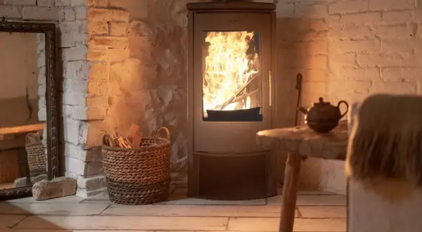 Un accogliente impianto riscaldamento a legna con fiamme vive, cesto di legna e teiera su un tavolino rustico.