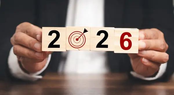 Ręce trzymają kostki z napisem "2026" i tarczą celowniczą. To symboliczne przedstawienie celów i planowania, jak środki trwałe co to, w kontekście przyszłości.