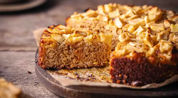 Ein saftiger Haferflocken Kuchen mit Apfelstücken, auf einem Holzbrett, bereit zum Genießen.