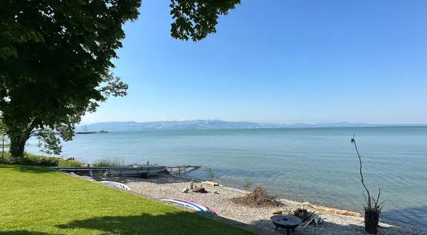 Słoneczny dzień nad Jeziorem Bodeńskim. Plaże z kamykami, łodzie i zielona trawa zapraszają do relaksu.