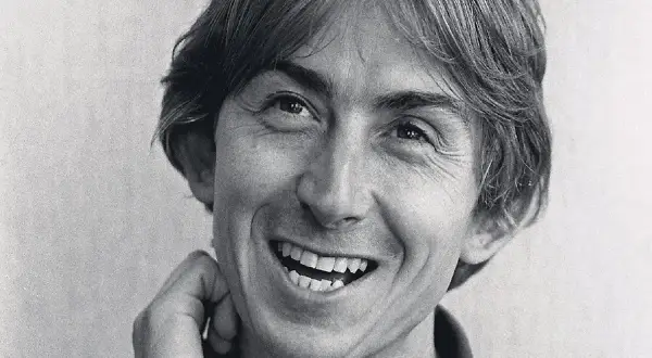 Black and white close-up portrait of Mark Hollis of Talk Talk smiling with his hand near his face.