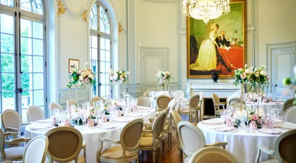 Salle de réception élégante avec tables rondes dressées pour un mariage. Un tableau ancien domine la pièce, offrant une idée de plan de table mariage.