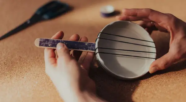 Ręce składają prosty instrument perkusyjny: patyczek z ozdobnym papierem i miseczka z gumkami. Oto jak zrobić instrument perkusyjny!