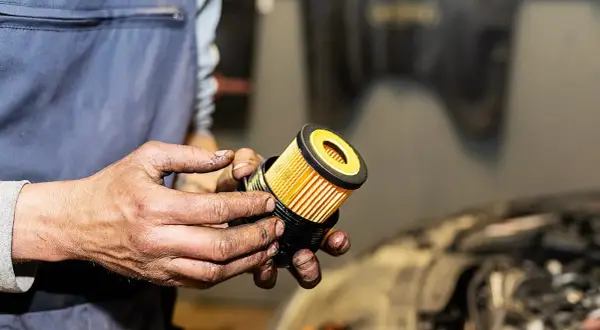 Hände halten einen neuen, gelben Ölfilter für ein Auto.