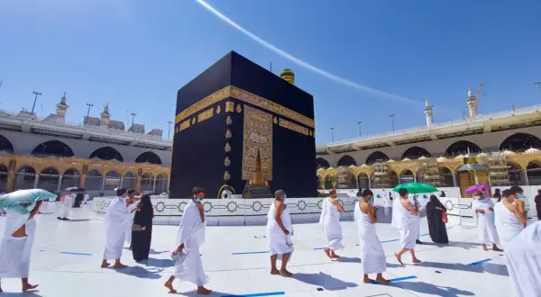 Pielgrzymi w białych strojach okrążają Kaabę, święte miasto islamu, w słoneczny dzień.