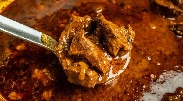 Ein Löffel voller herzhaftem Wildschwein Gulasch, das in einer reichen, dunklen Sauce schmort.