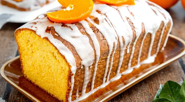 Omas saftiger Orangenkuchen, mit Zuckerguss und frischen Orangenscheiben garniert, duftet herrlich auf dem rustikalen Holztisch.