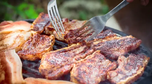 Soczysty boczek na grillu, idealny po marynacie. Dwie widelce pomagają w obracaniu kawałków.