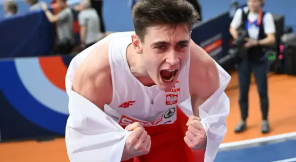 Młody lekkoatleta w biało-czerwonej koszulce okryty białą flagą, krzyczy z radości po zwycięstwie na halowych mistrzostwach europy lekkoatletyka.