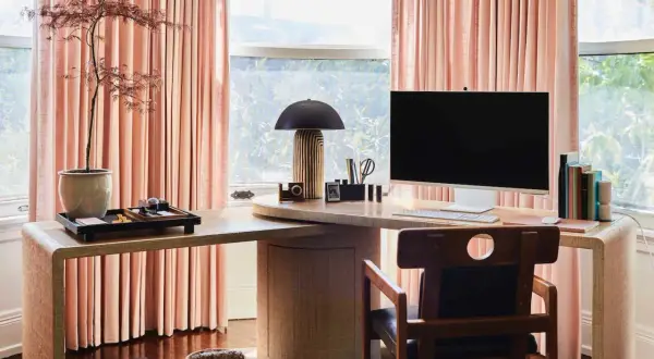 Stylish personal office decor ideas: a modern desk with a computer, lamp, and plant, framed by soft pink curtains.