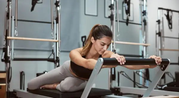 Kobieta ćwiczy na reformerze pilates. Czy to lepsze na kręgosłup niż joga?