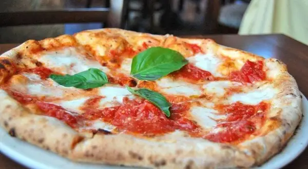 Une délicieuse margarita pizza, avec sa croûte dorée, sa sauce tomate vibrante et son fromage fondant, garnie de feuilles de basilic frais.
