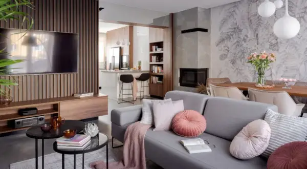 Nowoczesny salon z szarą sofą, kominkiem i otwartą kuchnią. Galeria wnętrz zachwyca detalami.