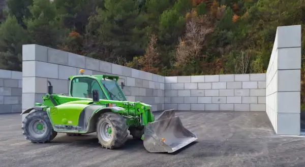 Chargeuse verte dans un espace clos de murs en blocs de béton, prêt pour le silo ensilage.