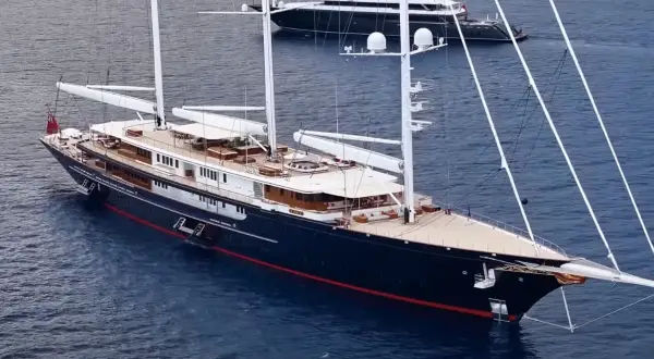 Il maestoso yacht Koru, con i suoi lussuosi interni, naviga in acque blu. Un altro yacht più piccolo è visibile sullo sfondo.