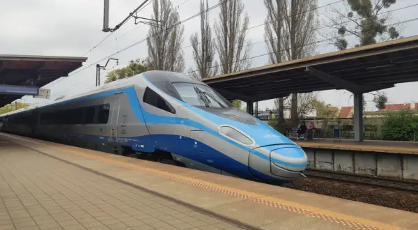 Nowoczesny eip pociąg Pendolino stoi na peronie. W tle widać wiatę, drzewa i budynki.