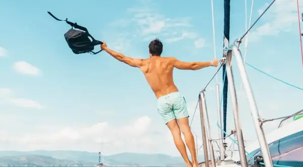Uomo con zaino in barca a vela, un esempio di come vestirsi in barca a vela: costume e libertà.