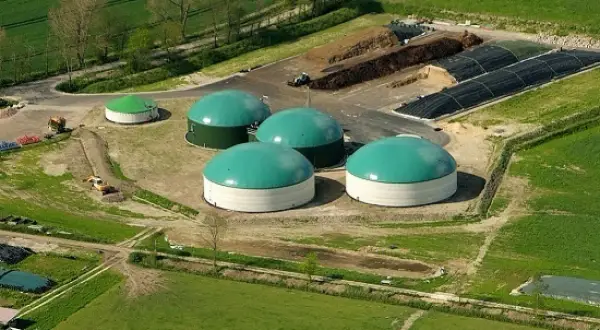 Impianto di biogas con grandi serbatoi verdi e bianchi, cumuli di materiale organico e serre. Un esempio di incentivi biogas per l'energia rinnovabile.