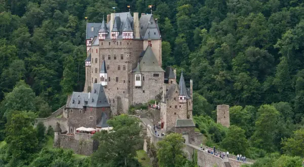 Burg Eltz, ett sagoslott omgivet av grönskande skog, reser sig stolt på en klippa. Många besökare vandrar längs murarna.
