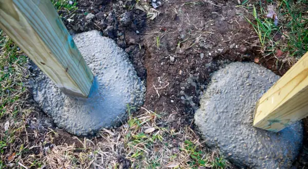 Zwei Holzpfosten werden in frisch gegossenen Beton gesetzt, um einen stabilen Zaun zu bauen. Das Einbetonieren der Pfosten sorgt für Langlebigkeit.