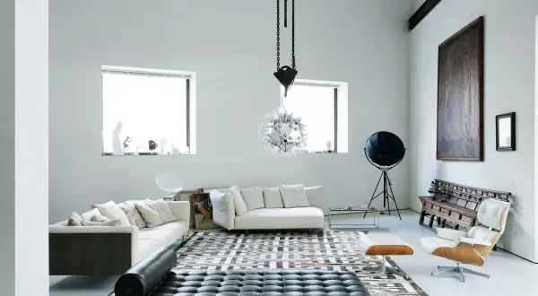 Soggiorno moderno con divani bianchi, chaise longue in pelle nera e un'iconica poltrona. Un ambiente che evoca case eleganti e raffinate.
