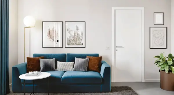 Divano blu intenso con cuscini tortora e grigi. Un tavolino bianco e un tappeto scuro completano l'ambiente.