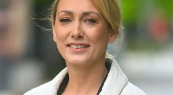 Portret uśmiechniętej blondynki w jasnym płaszczu.