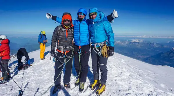 Drei Bergsteiger auf dem Gipfel des Monte Blanc, umgeben von Schnee und einer atemberaubenden Aussicht.