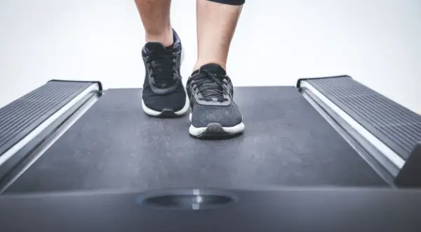 Nogi w sportowych butach stawiają pierwsze kroki na bieżni w bloku.