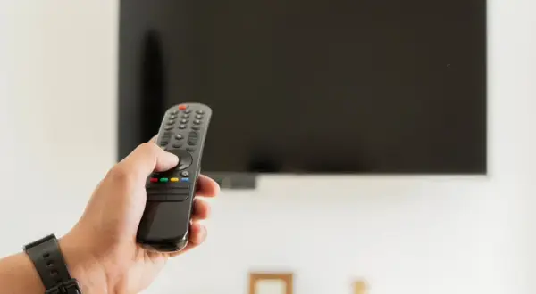 Dłoń trzymająca pilot do telewizora, zastanawiająca się, czy telewizor pobiera dużo prądu.