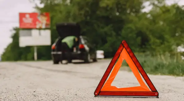 Trójkąt ostrzegawczy na drodze, obok samochodu z otwartym bagażnikiem. Awaria samochodu w terenie zabudowanym.