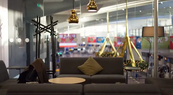 Mysig lounge med soffor, bord och lampor. En jacka hänger på en klädhängare. Utsikt över flygplatsen från Pearl Lounge Arlanda.