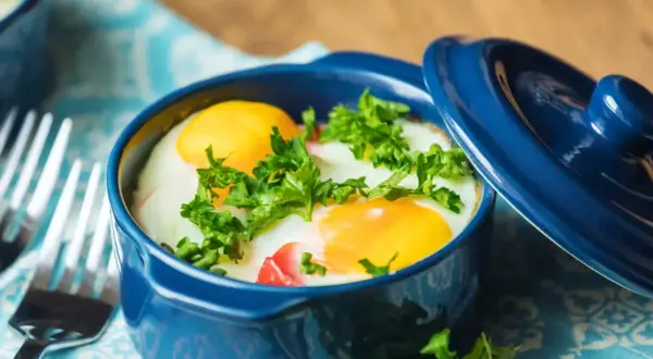 Un délicieux oeuf cocotte, deux jaunes d'œufs brillants dans leur ramequin bleu, parsemé de persil frais. Prêt à être dégusté !