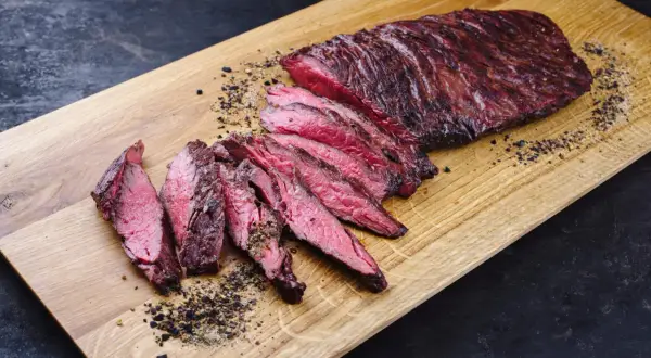 Perfekt zubereitetes Skirt Steak, in Scheiben geschnitten, liegt auf einem Holzbrett. Gewürze und Pfeffer sind verstreut.