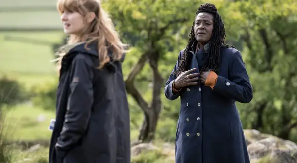 Två kvinnor i mörka rockar utomhus, en med blont hår, den andra med dreadlocks. Scen från engelska kriminalserier.