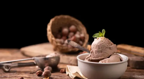 Delizioso gelato alla nocciola appena fatto con la gelatiera, guarnito con menta fresca. Nocciole in un cesto sullo sfondo.