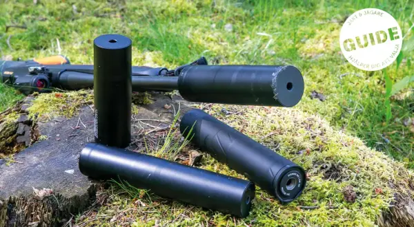 Tre ljuddämpare för jakt, en 125 mm, ligger på en mossig stubbe bredvid ett gevär. En guide hjälper dig att välja rätt.