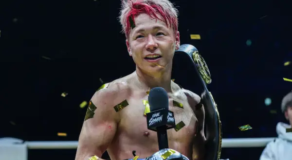 Fighter with red-streaked hair holds a championship belt, confetti falling. This victory might be the tko retirement meaning for his career.