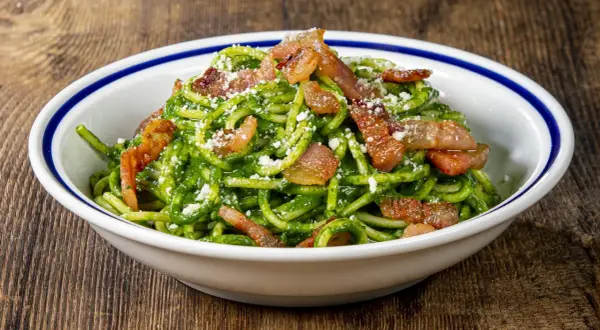 Un piatto invitante di pasta con spinaci e croccante pancetta, cosparso di formaggio grattugiato.