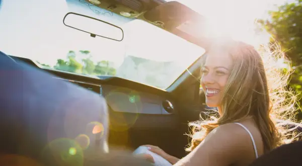 Vrolijke vrouw in cabriolet, haar haar wappert in de zon. Ze lacht, niet te streng voor jezelf, genietend van de rit.