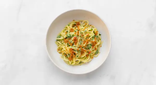 Spaghetti alla carrettiera mit frischer Petersilie, Chili und knusprigen Semmelbröseln in einer weißen Schüssel auf Marmor.