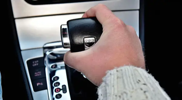 Dłoń trzymająca dźwignię zmiany biegów w samochodzie z napisem DSG. Widoczne przyciski ESP, Auto Hold i P.