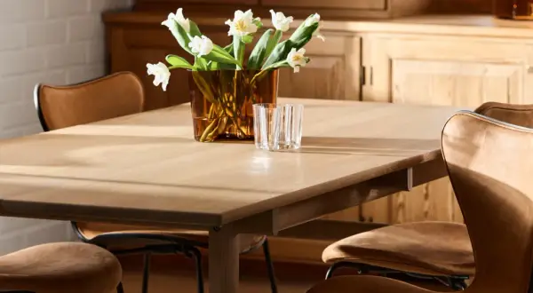 Ett ljust träbord med klassiska designstolar i läder. En vas med vita blommor och glas står på bordet.