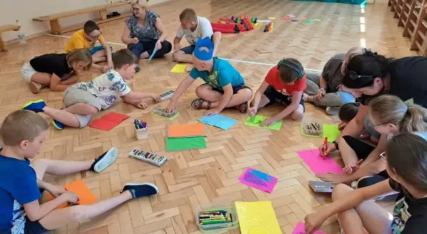 Dzieci klas 1-3 biorą udział w zabawach integracyjnych, rysując na kolorowych kartkach.