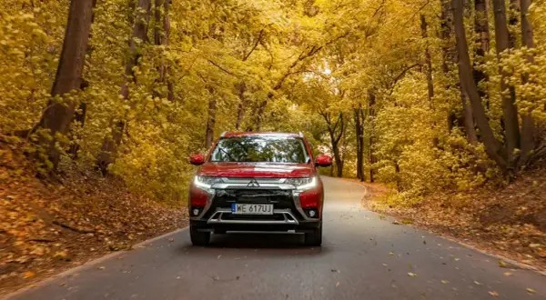 Czerwony Mitsubishi Outlander na jesiennej drodze wśród złotych liści. Sprawdź jego spalanie w podróży!