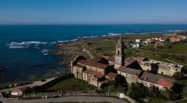 Vista aérea del Monasterio de Santa María de Oia, con el mar azul al fondo y campos verdes.