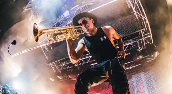 Timmy Trumpet gra na trąbce na scenie w Polsce, otoczony dymem i światłami.