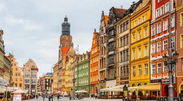 Bunte Häuserfronten am Wroclaw Rynek, mit einem markanten Turm im Hintergrund. Menschen spazieren über den gepflasterten Platz.